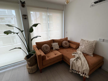 Un sillón esquinero tapizado en pana color terracota, decorado con almohadones tejidos en tonos neutros y una manta clara, que crean un ambiente cálido y natural en el living