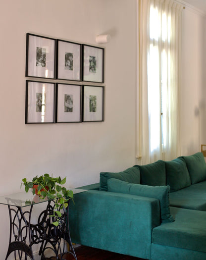 Sillón en forma de herradura tapizado en tela verde oscuro, con cojines a juego, ubicado en una sala con piso de madera y mesas de centro redondas con superficie de mármol