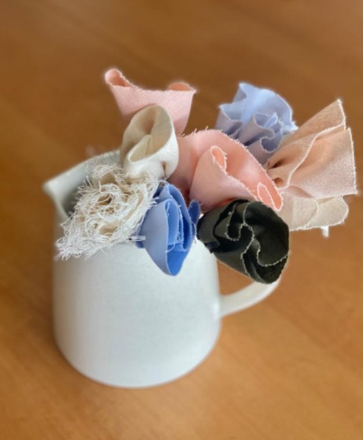 Flores de lino rosa, celeste, crema y negra con bordes deshilachados en una jarra de cerámica blanca