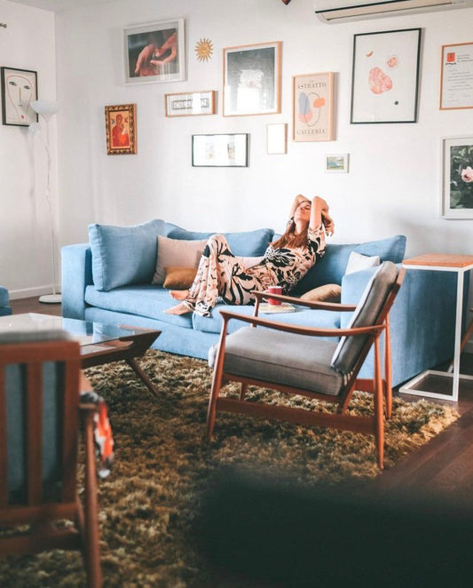 Living de Josefina Álvarez Castillo con su sofá esquinero azul, una butaca de madera y una pared de cuadros