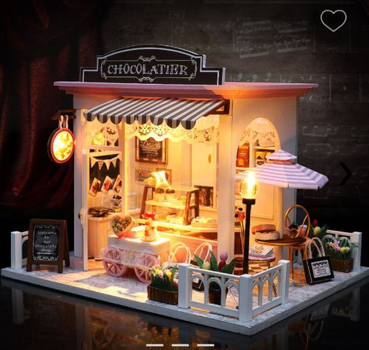 Chocolatería en miniatura armada, con toldo a rayas, vidriera iluminada, vereda con sombrilla y farol