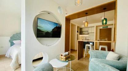 Living del departamento con televisor en hornacina circular, barra de madera con banquetas altas y un sillón Brigitte celeste