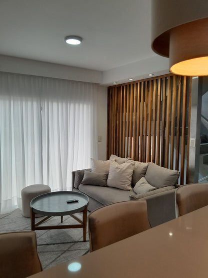 Vista del living de Arquitectura SN desde la barra: sofá a medida gris claro, puff redondo y separador de madera