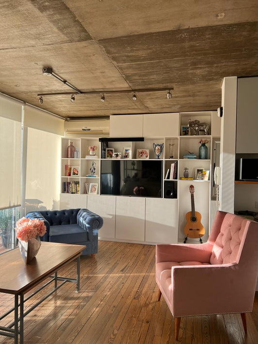 Living de Gigi con el Sillón Chesterfield azul, el Sillón Velvet rosa y una biblioteca blanca con TV