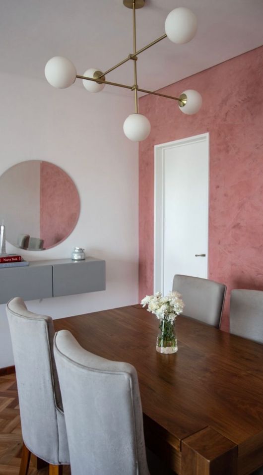 Comedor con pared rosa, mesa de madera y Sillas Amalfi grises, con espejo redondo y lámpara de globos, en Juramento