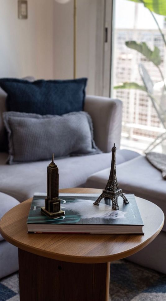 Detalle del Esquinero Elton gris con almohadones azules junto a una mesa de madera con una Torre Eiffel decorativa