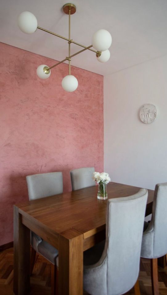 Mesa de madera con Sillas Amalfi grises bajo una lámpara de globos, en el comedor con pared rosa de Juramento