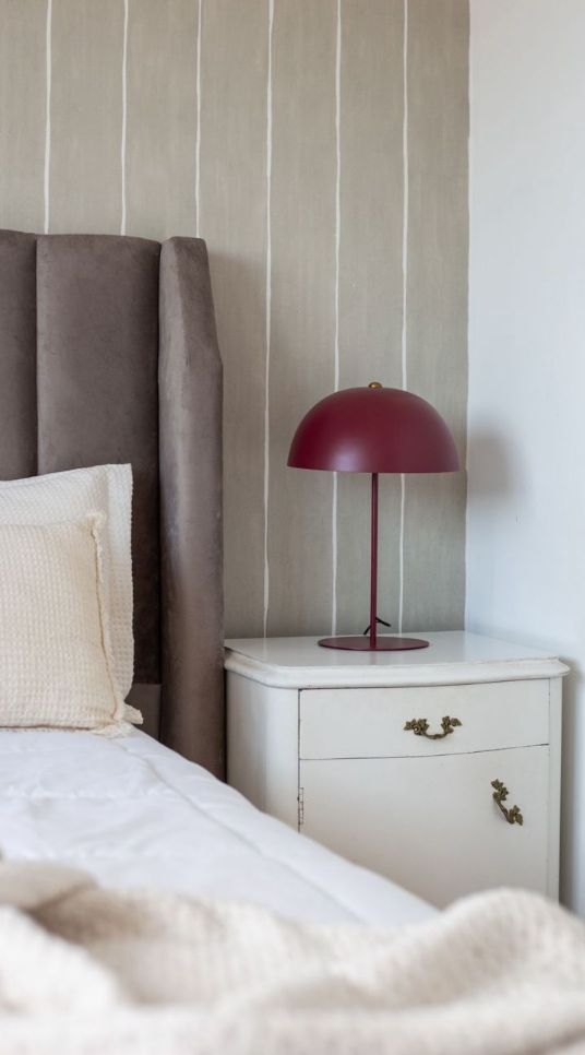 Oreja lateral del Respaldo Alpes gris junto a una mesa de luz blanca con lámpara bordó