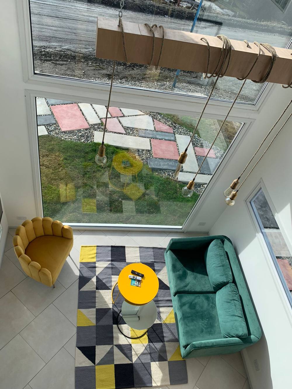 Vista desde arriba del loft en Ushuaia con el Sofá Corina verde, el Sillón Angie mostaza y la alfombra geométrica