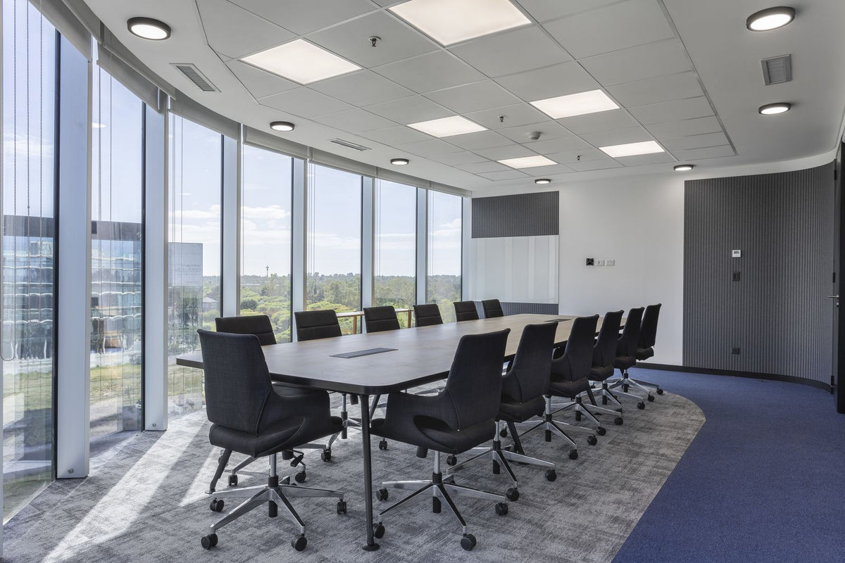Sala de directorio con mesa de reunión Avant de Archivos Activos larga, tapa gris y sillas negras junto a ventanales