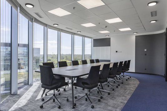 Sala de directorio con mesa de reunión Avant de Archivos Activos larga, tapa gris y sillas negras junto a ventanales