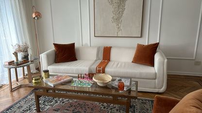 Sofá bouclé color crudo a medida con almohadones de terciopelo terracota y una manta, en el living de Milagros Maylin