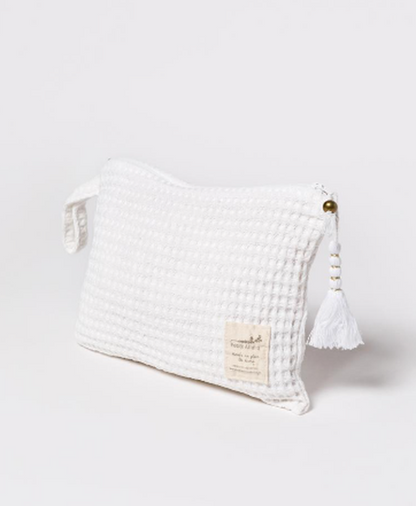 Necessaire Off White de wafle de Petite Affaire con borla blanca y cuentas, sobre fondo claro