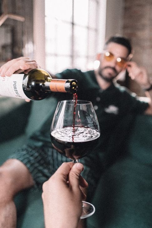 Pirovano llenando una copa de vino tinto, sentado en su Esquinero Elton verde inglés