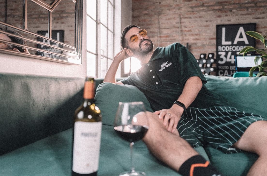 Pirovano recostado en su Esquinero Elton de terciopelo verde inglés, con una copa y una botella de vino tinto