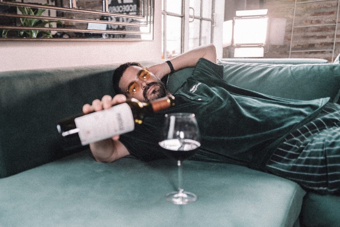 Pirovano recostado a lo largo del chaise de su Esquinero Elton verde inglés, con una botella de vino