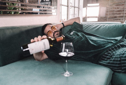 Pirovano recostado a lo largo del chaise de su Esquinero Elton verde inglés, con una botella de vino