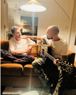 Abel Pintos con su guitarra en el Sofá Elton color ladrillo de su living, junto a otra persona