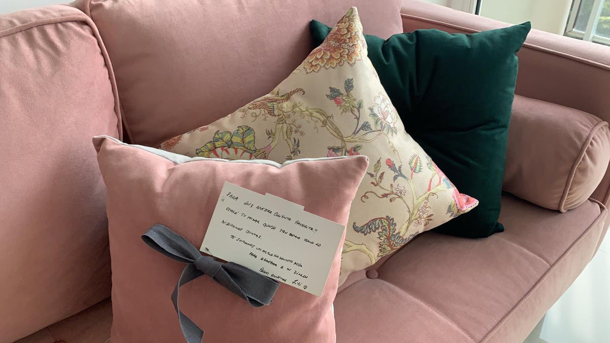 Almohadones decorativos sobre el sillón esquinero rosa, con una tarjeta manuscrita de agradecimiento para Lu.