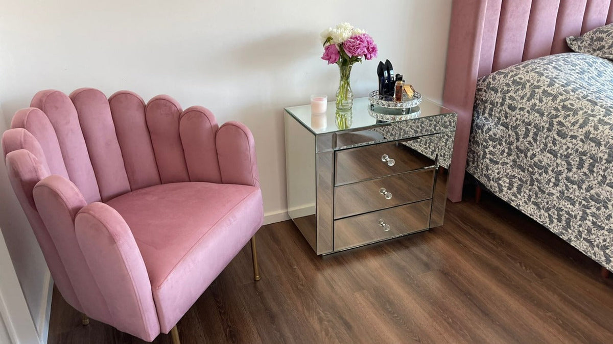 Sillón Angie rosa con forma de concha y patas doradas, junto a la mesita espejada y el Respaldo Alpes rosa del dormitorio de Simone