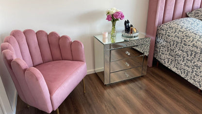 Sillón Angie rosa con forma de concha y patas doradas, junto a la mesita espejada y el Respaldo Alpes rosa del dormitorio de Simone
