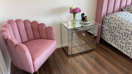 Sillón Angie rosa con forma de concha y patas doradas, junto a la mesita espejada y el Respaldo Alpes rosa del dormitorio de Simone