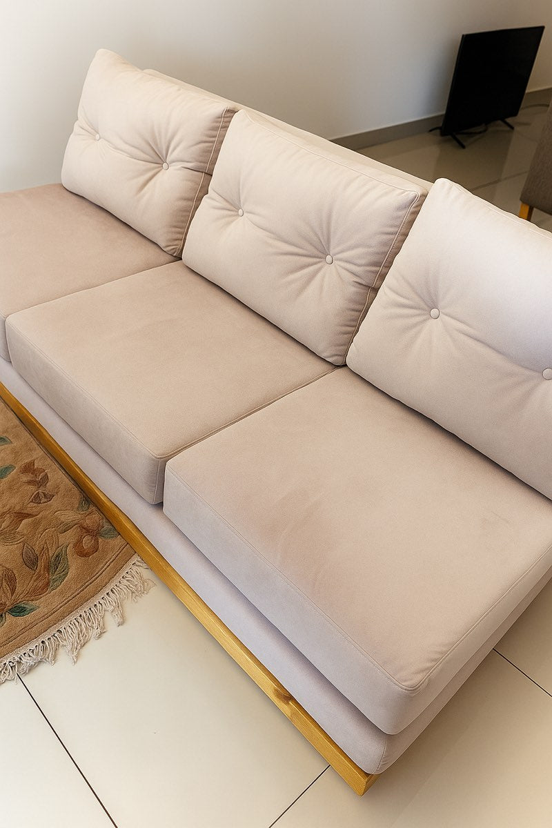 Sofá Cardiff sin apoyabrazos tapizado en crema, con base de madera a la vista, en el living del departamento de Caballito