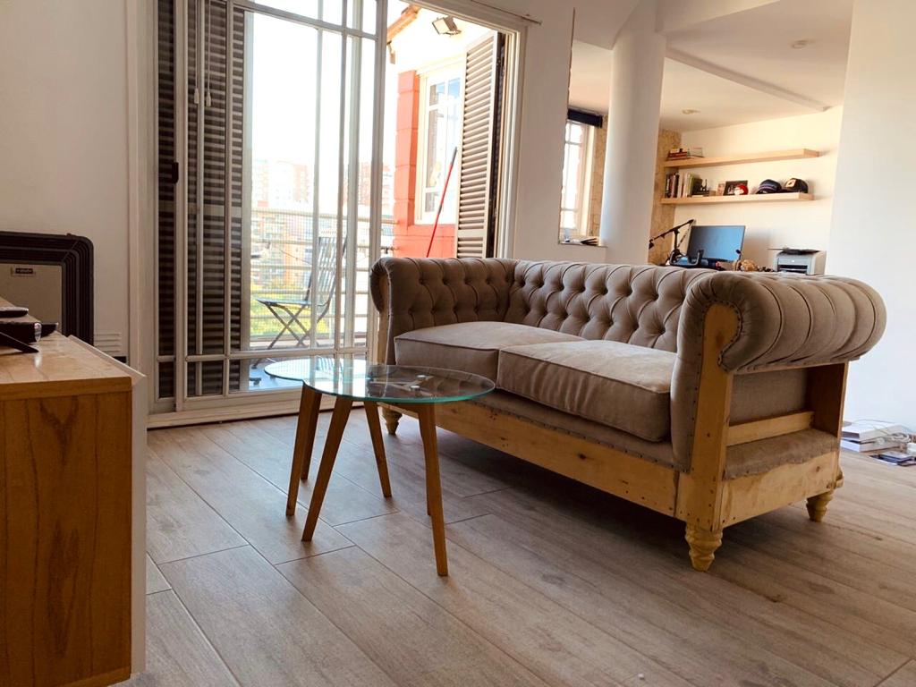 Sofá Deconstructed beige con capitoné y base rústica a la vista, junto a la mesita de Maxi