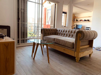 Sofá Deconstructed beige con capitoné y base rústica a la vista, junto a la mesita de Maxi