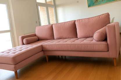 Sillón esquinero Bambú tapizado en rosa viejo, con capitoné en el asiento, almohadones cilíndricos y patas de madera torneada, en el living de Lu.