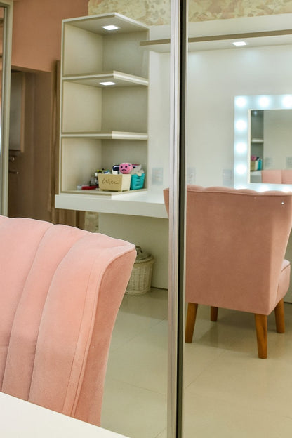 Detalle del Sillón Angie en beige, con su estructura curvada y patas doradas, junto a la ventana de la habitación.