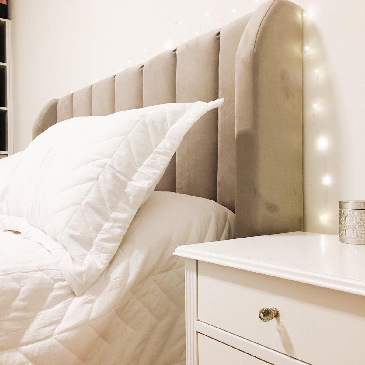 Respaldo Alpes gris junto a la mesa de luz blanca, en el dormitorio de Martha