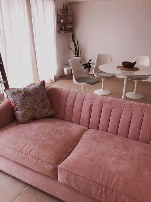 Sofá Mila tapizado en terciopelo rosa, con respaldo acanalado vertical, junto al comedor con mesa y sillas Saarinen en el living de Gaby