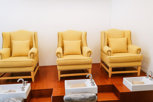 Tres Sillones Flower tapizados en amarillo mostaza, con tachas doradas y patas de madera con travesaño, integrados como sillones de pedicura en el spa de Sofía en Santa Fe.