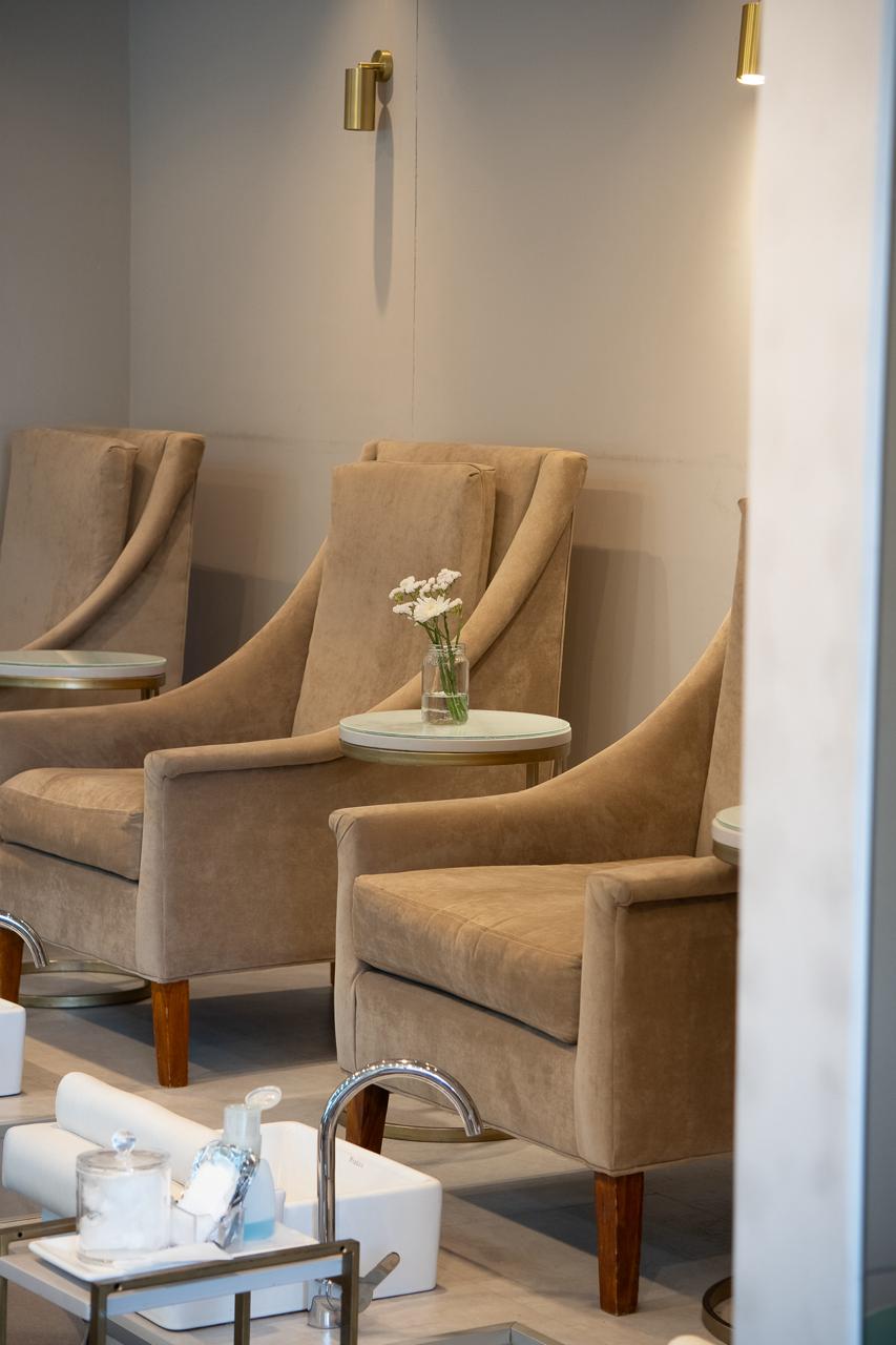 Sillones Bélgica tapizados en tono taupe, con patas de madera, alineados en el salón de Rebecca Nail Bar