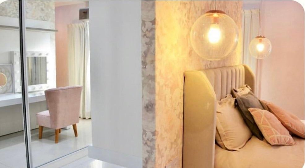 Respaldo Alpes beige con lámparas colgantes junto a la cama, y el rincón de maquillaje reflejado en el espejo
