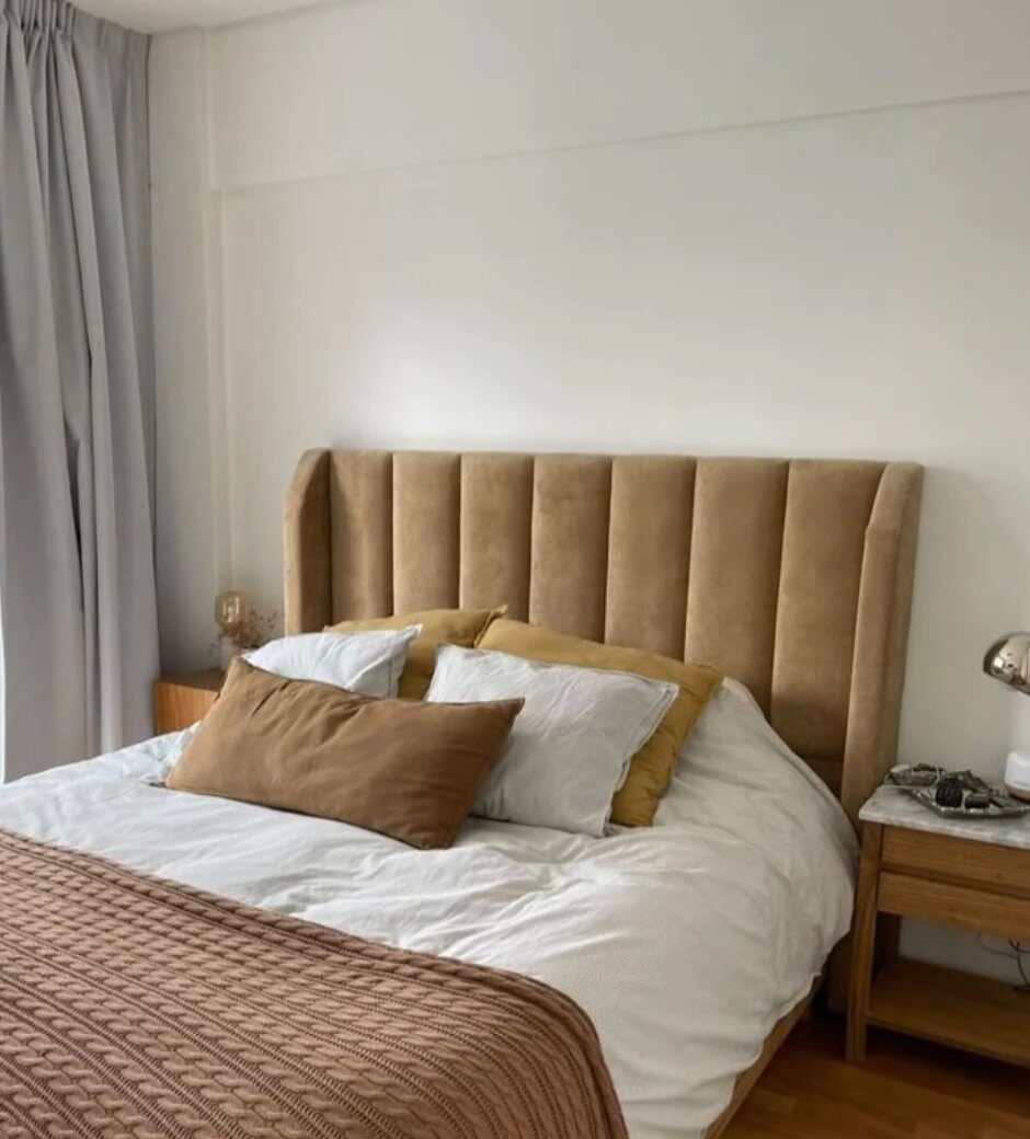 Respaldo Alpes caramel con canales verticales y orejas laterales, junto a una mesa de luz de madera con tapa de mármol, en el dormitorio de Paola
