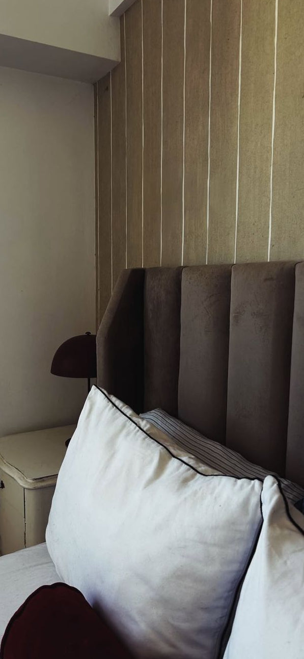 Respaldo Alpes en gris pardo con canales verticales, contra la pared de listones de madera del dormitorio de Tomás