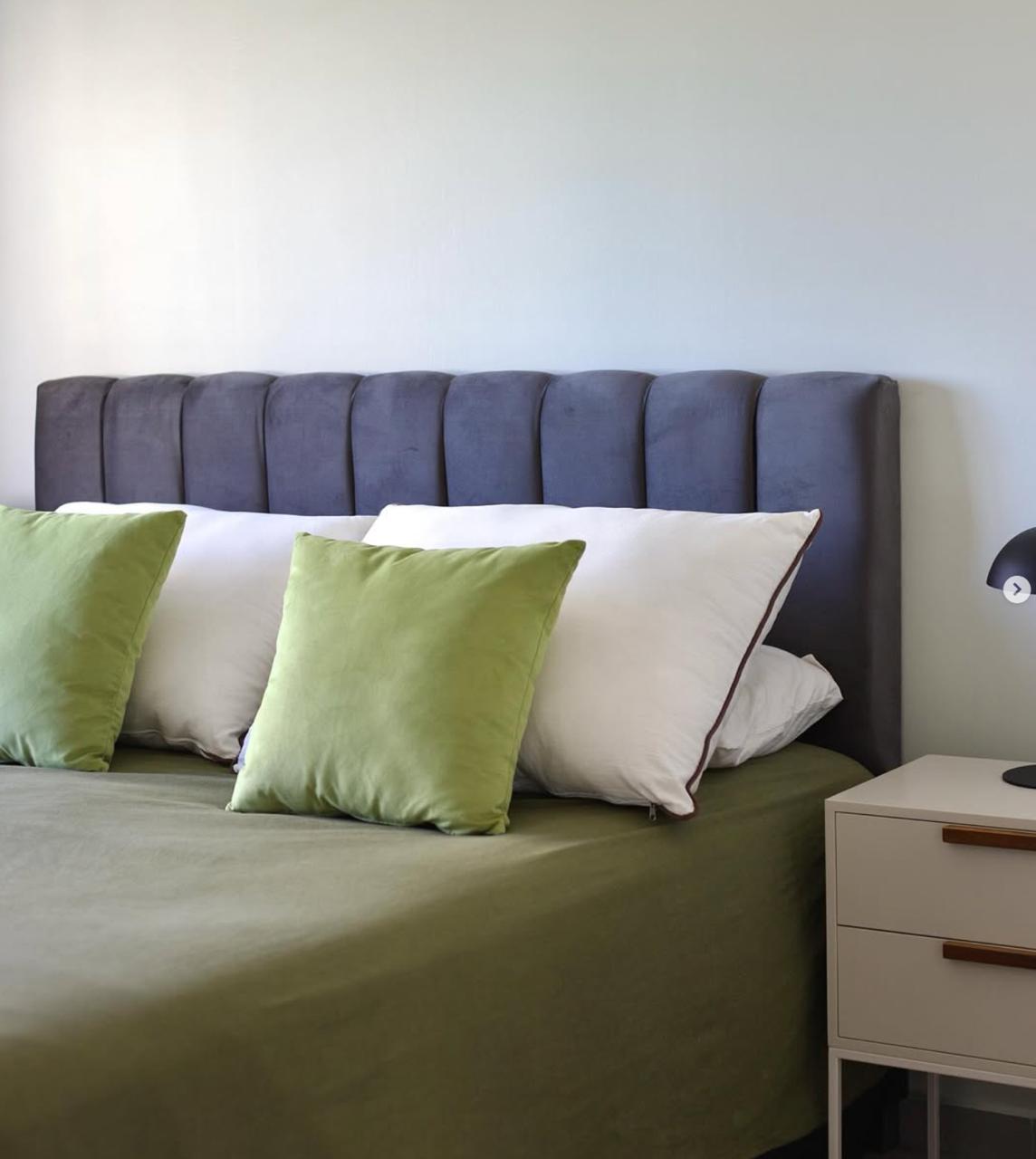 Respaldo Alpes gris de canales verticales, hecho sin orejas, con almohadones verdes y mesa de luz blanca, en el dormitorio de Simón decorado con WN Interiores