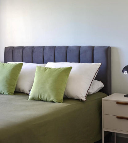 Respaldo Alpes gris de canales verticales, hecho sin orejas, con almohadones verdes y mesa de luz blanca, en el dormitorio de Simón decorado con WN Interiores