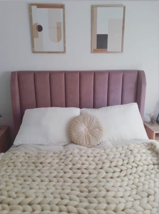 Respaldo Alpes rosa malva con canales verticales y orejas laterales, con ropa de cama blanca y manta tejida, en el dormitorio de Celeste