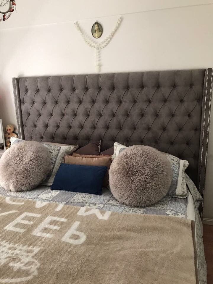 Respaldo Emmy gris con capitoné profundo, aletas laterales y tachas plateadas, detrás de la cama de Sol