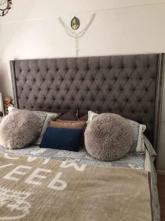 Respaldo Emmy gris con capitoné profundo, aletas laterales y tachas plateadas, detrás de la cama de Sol