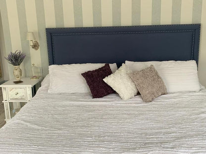 Vista del dormitorio de Patricia con el Respaldo Grace azul navy, almohadones con rosas y una mesa de luz blanca espejada