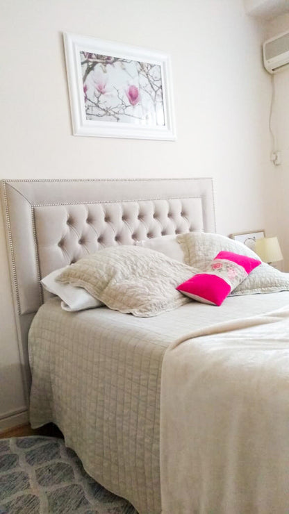 Respaldo Grace beige con capitoné y marco de tachas plateadas, con almohadones fucsia con rosas, en el dormitorio de Estefanía