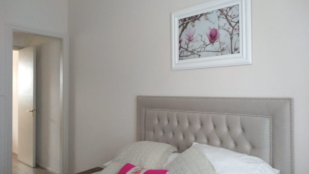 Vista general del Respaldo Grace beige con tachas plateadas bajo un cuadro de magnolias, en el dormitorio de Estefanía