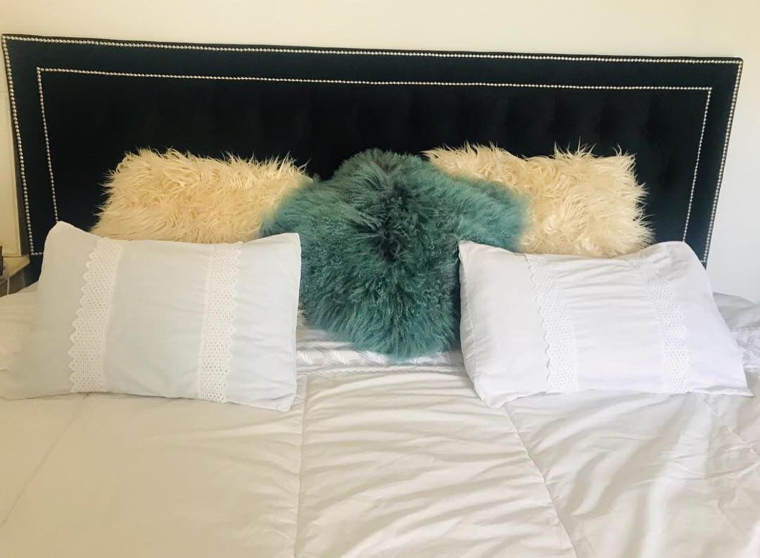 Respaldo Grace negro con capitoné y doble marco de tachas plateadas, con almohadones de pelo y ropa de cama blanca, en el dormitorio de Marisol