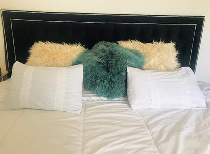 Respaldo Grace negro con capitoné y doble marco de tachas plateadas, con almohadones de pelo y ropa de cama blanca, en el dormitorio de Marisol