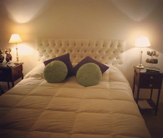 Respaldo Mily crema con capitoné en diamante, con almohadones verdes y morados y mesas de luz de madera, en el dormitorio de Valentina
