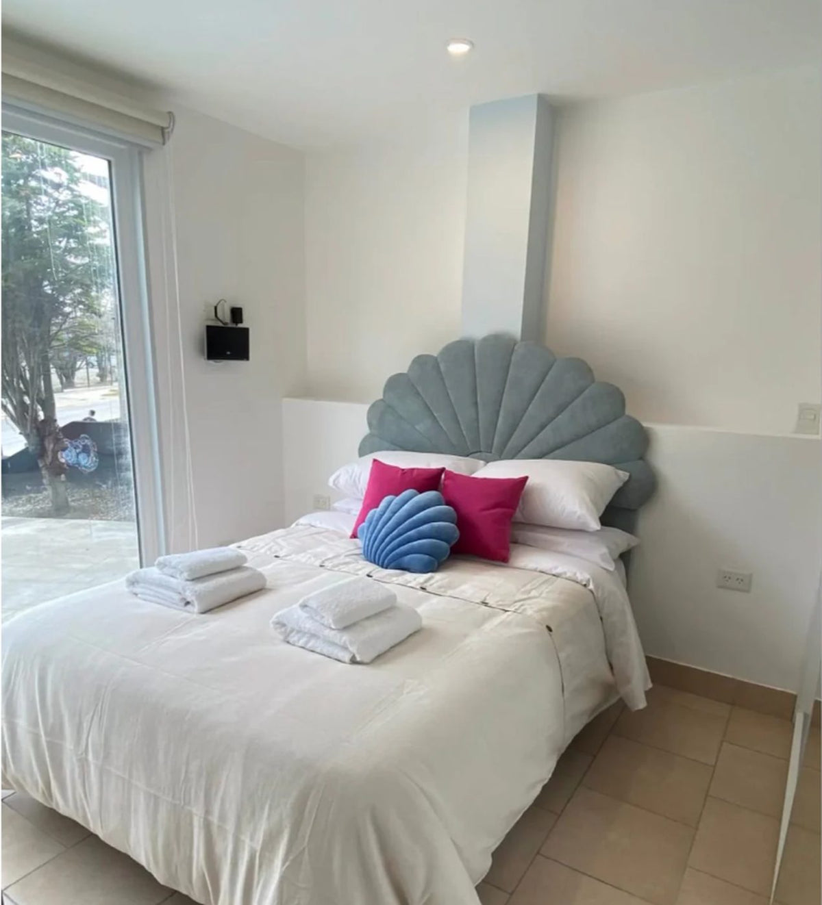 Respaldo de cama Ostras en verde agua, con sus gajos en forma de concha, detrás de una cama matrimonial de ropa blanca